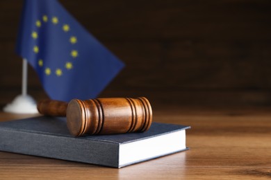 Photo of Judge's gavel and book on wooden table against European Union flag. Space for text