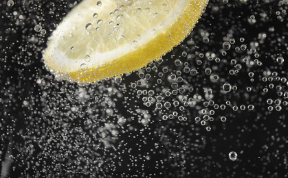 Juicy lemon slice in soda water against black background, closeup. Space for text