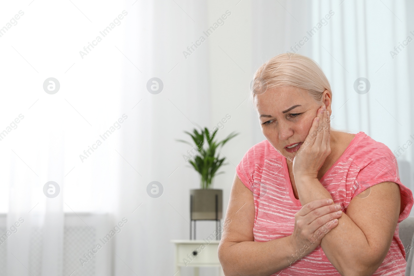 Photo of Mature woman suffering from strong tooth pain at home, space for text