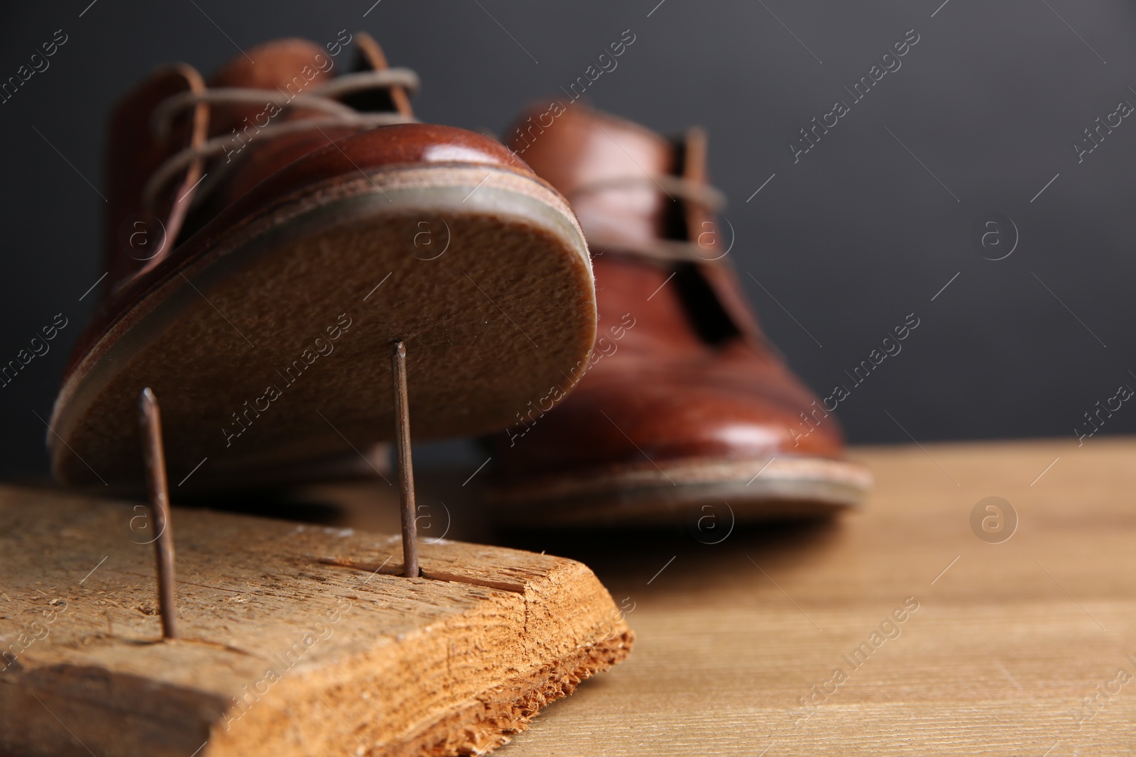 Photo of Metal nails in wooden plank and shoes on table, closeup