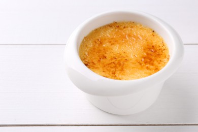 Photo of Delicious creme brulee in bowl on white wooden table, closeup