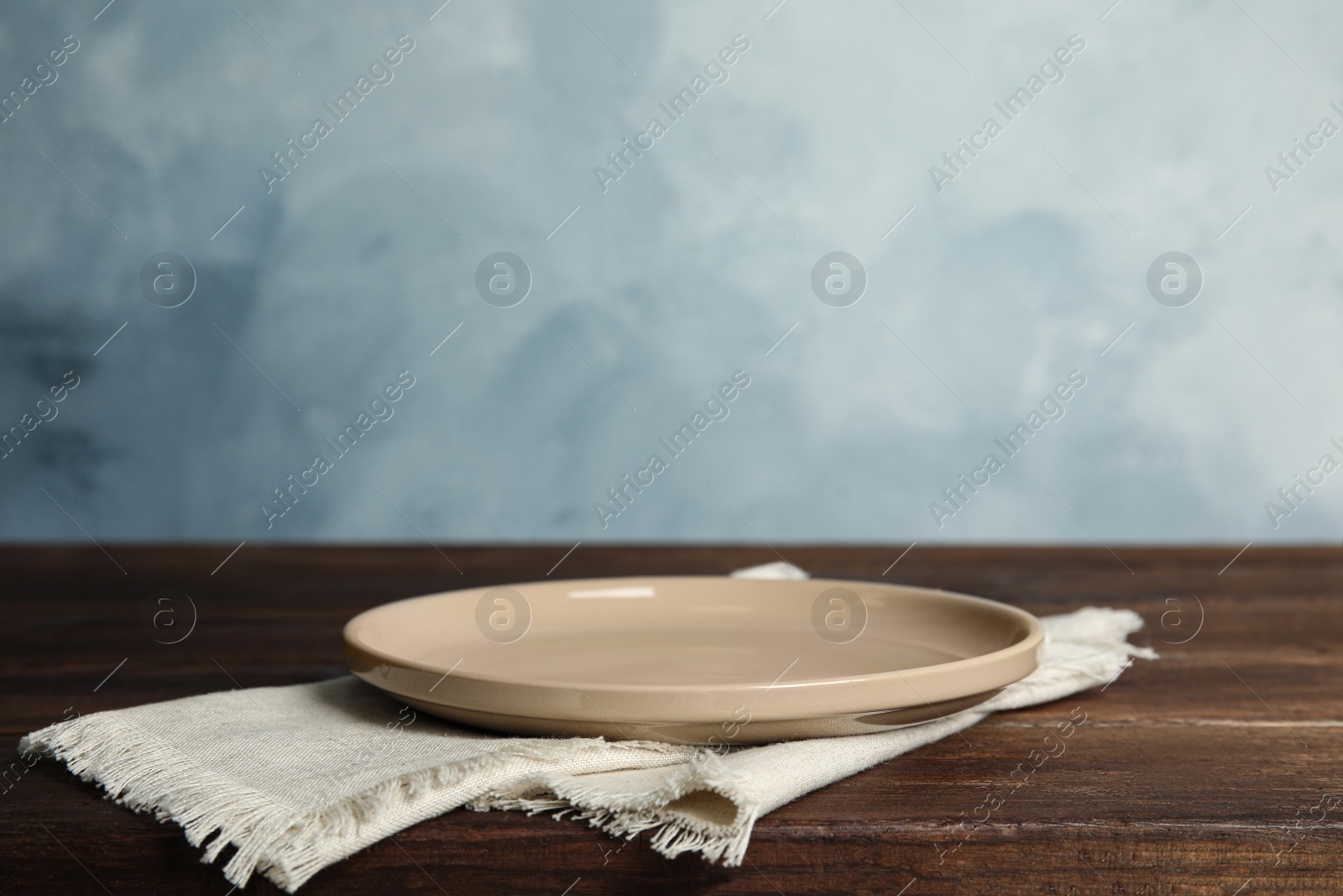 Photo of Empty plate and napkin on wooden table against light blue background. Space for text