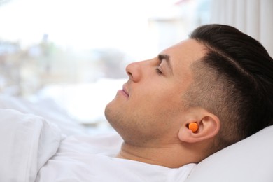 Photo of Man with foam ear plugs sleeping in bed, closeup