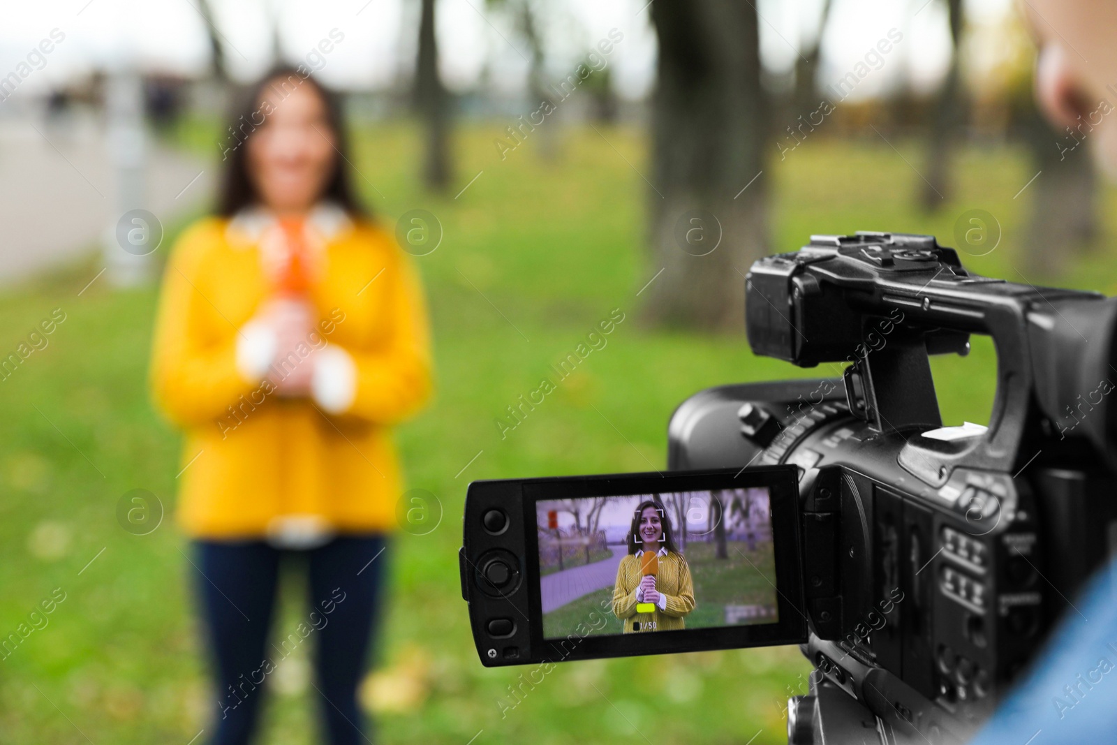 Photo of Young journalist and video operator working in park, focus on camera display