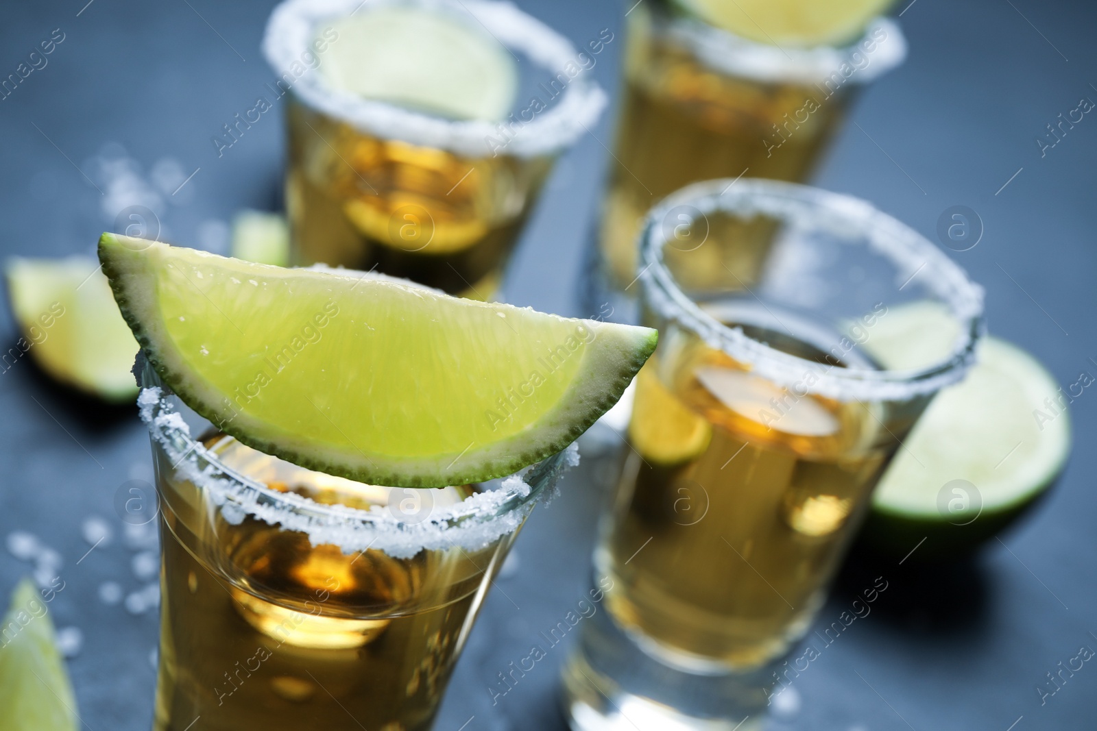 Photo of Mexican Tequila shots with salt and lime slices on grey table, closeup