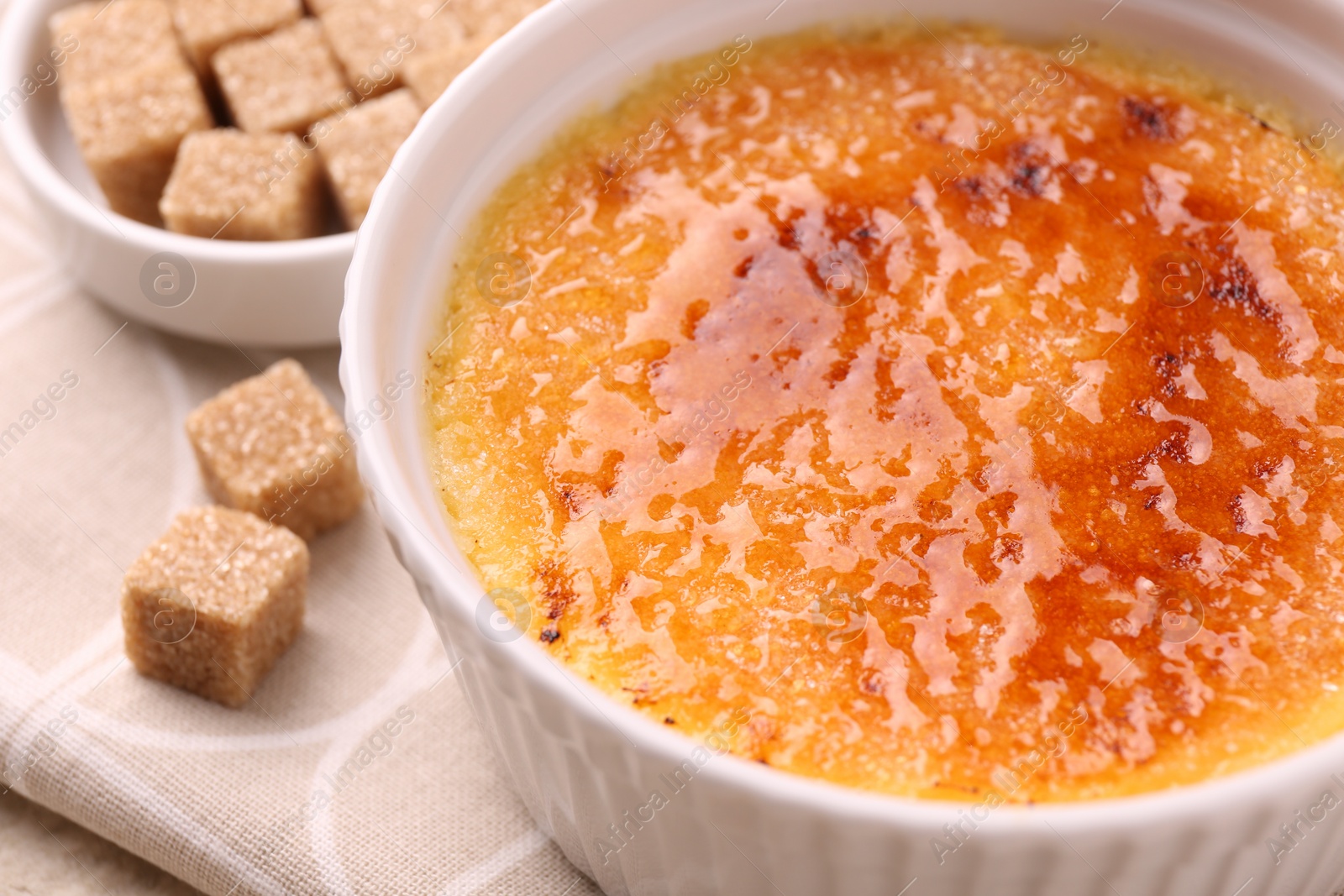 Photo of Delicious creme brulee in bowl and sugar cubes on table, closeup