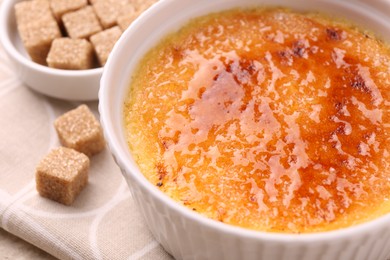 Delicious creme brulee in bowl and sugar cubes on table, closeup