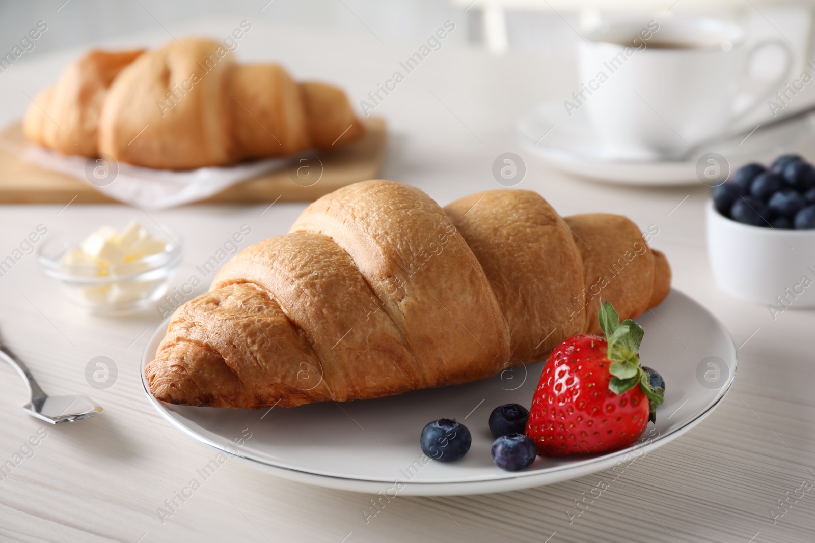 Photo of Plate with fresh crispy croissant and berries on white wooden table