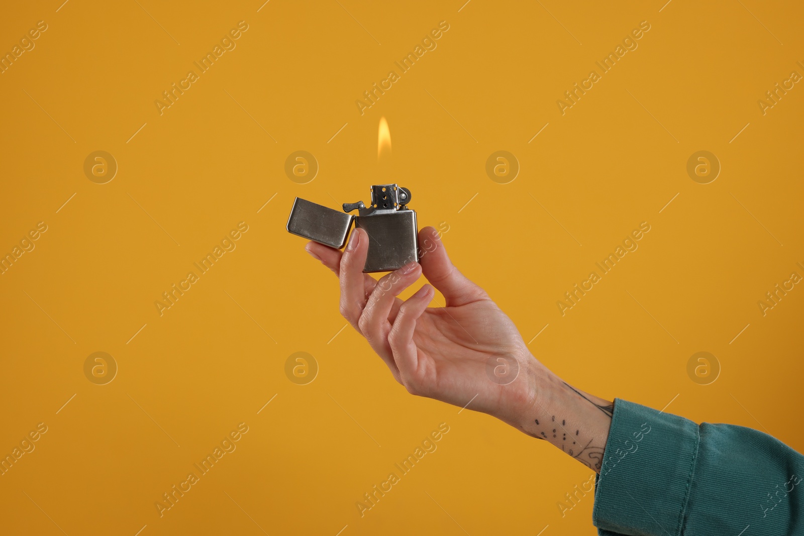 Photo of Woman holding lighter with burning flame on orange background, closeup