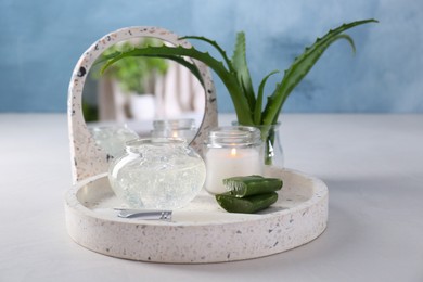 Jar of natural gel, burning candle, makeup brushes and fresh aloe leaves on white table