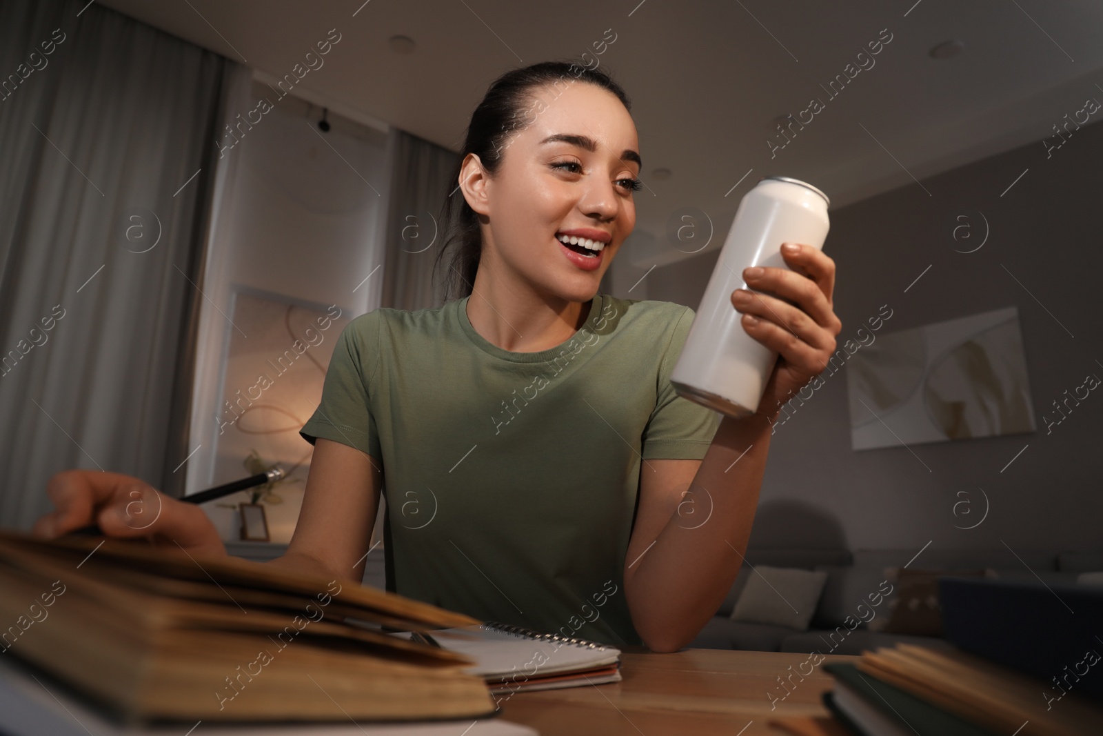 Photo of Emotional young woman with energy drink studying at home