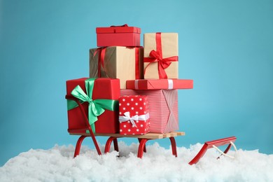 Photo of Sleigh with Christmas gift boxes and artificial snow on light blue background