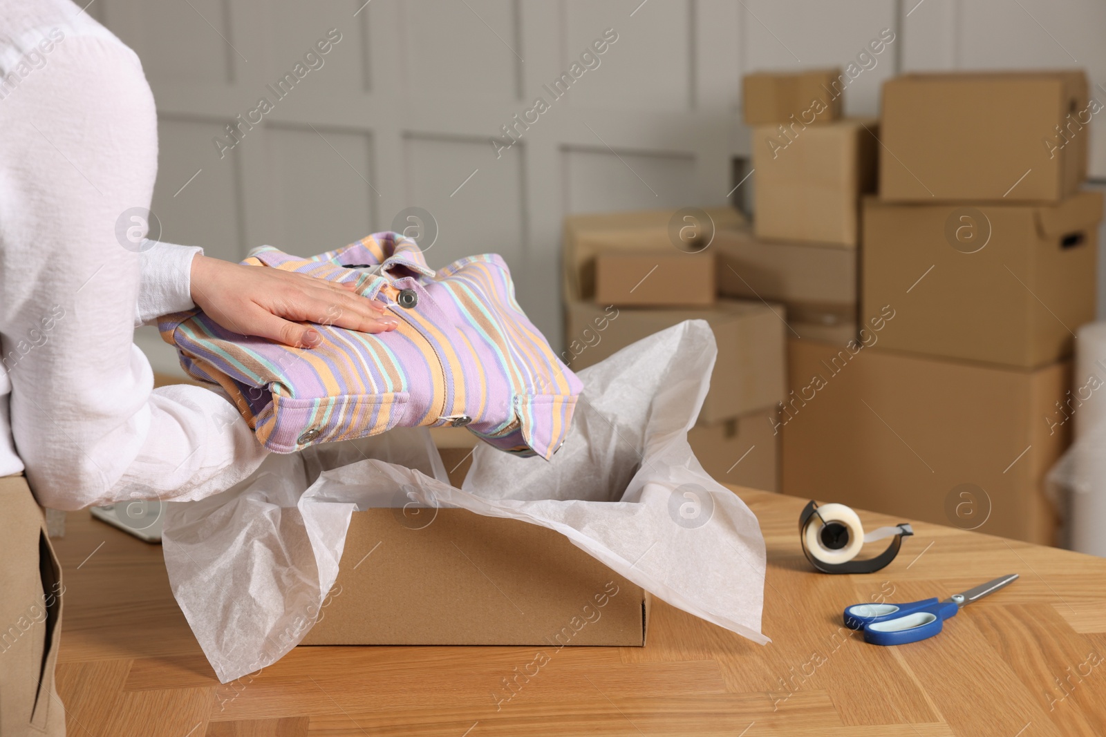 Photo of Seller packing shirt into cardboard box at table in office, closeup