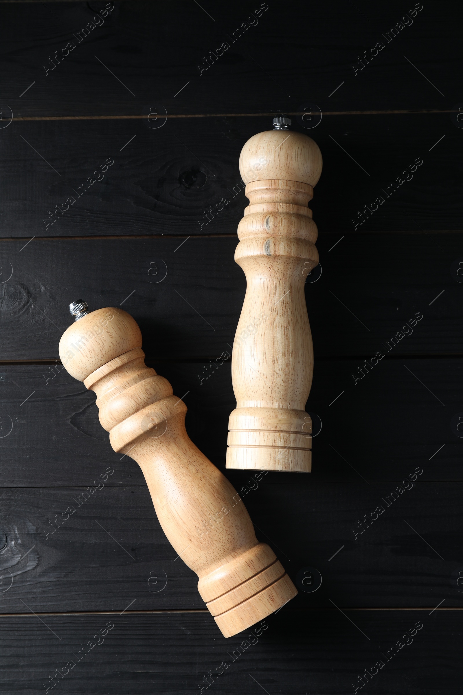 Photo of Salt and pepper shakers on black wooden table, flat lay