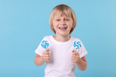Photo of Happy little boy with bright lollipops on light blue background