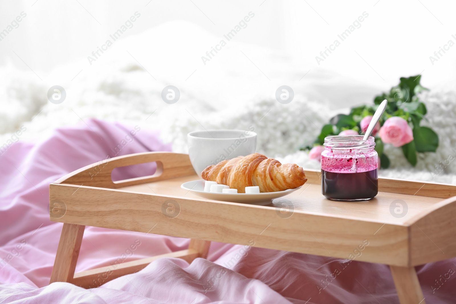 Photo of Wooden tray with tasty croissant, cup of coffee and jam on bed