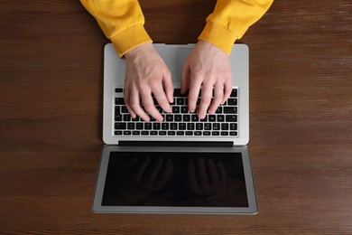 Man working with laptop at wooden table, top view