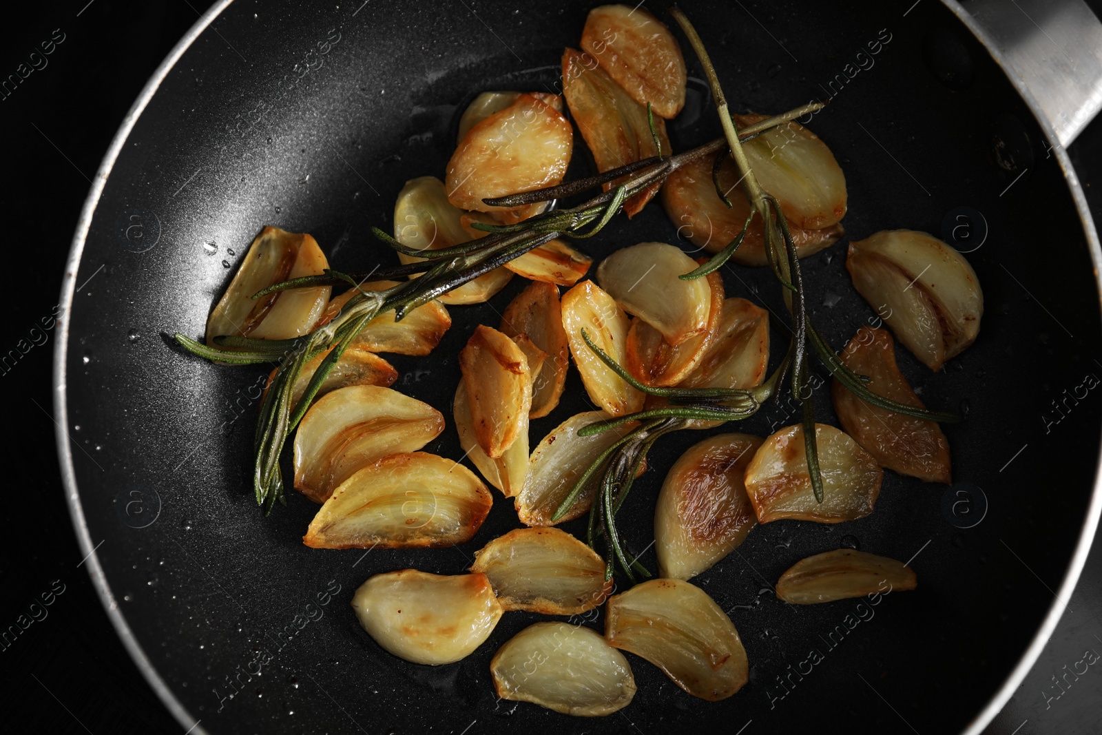 Photo of Frying pan with fried garlic cloves and rosemary, top view
