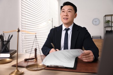 Happy notary writing notes at wooden table in office