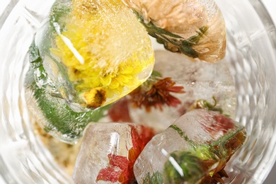 Photo of Glass of ice cubes with flowers, closeup view