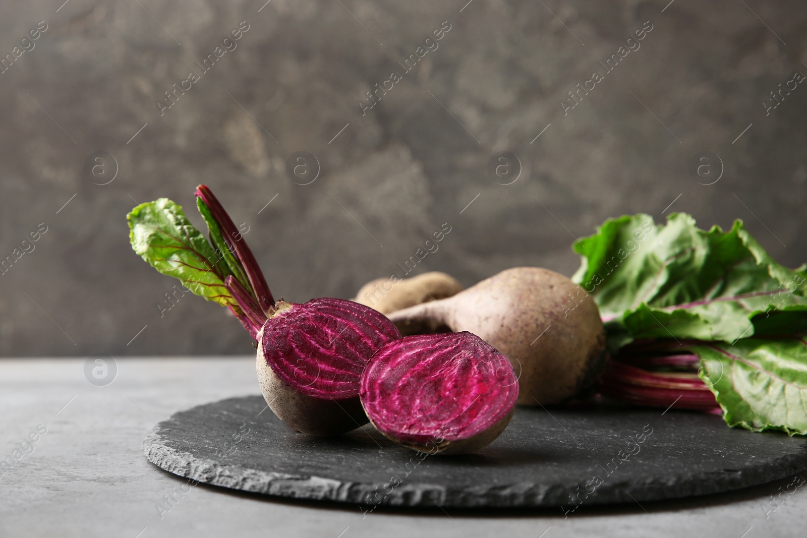 Photo of Slate board with fresh beets on table against grey background. Space for text