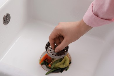 Photo of Woman putting vegetable scraps in garbage disposal at home, closeup