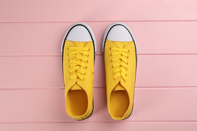 Photo of Pair of yellow sneakers on pink wooden table, flat lay