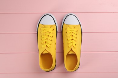 Pair of yellow sneakers on pink wooden table, flat lay