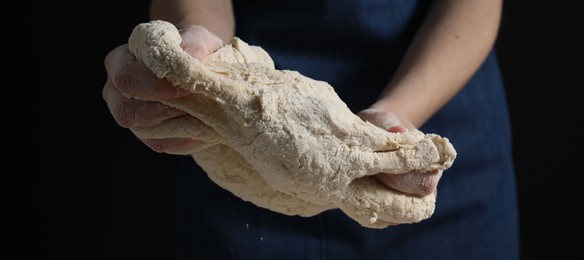 Photo of Making bread. Woman kneading dough on dark background, closeup