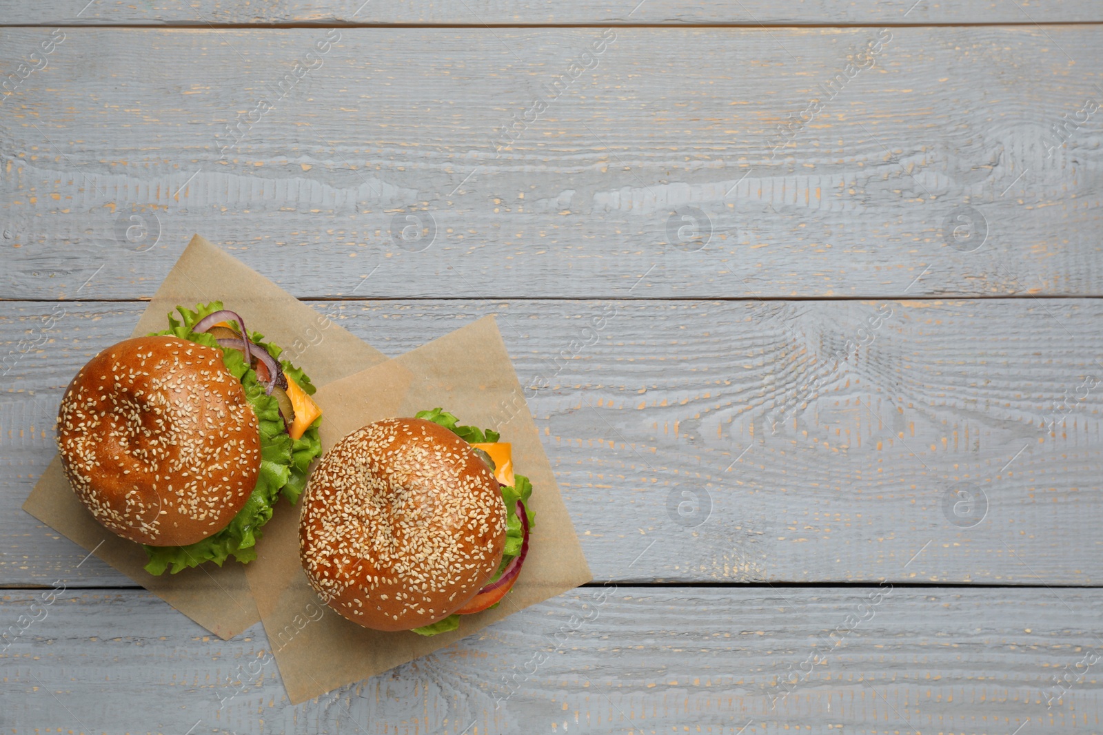 Photo of Tasty burgers on grey wooden table, top view. Space for text. Fast food