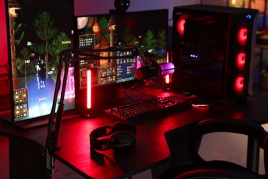 Photo of Playing video games. Modern computer, microphone and headphones on table indoors