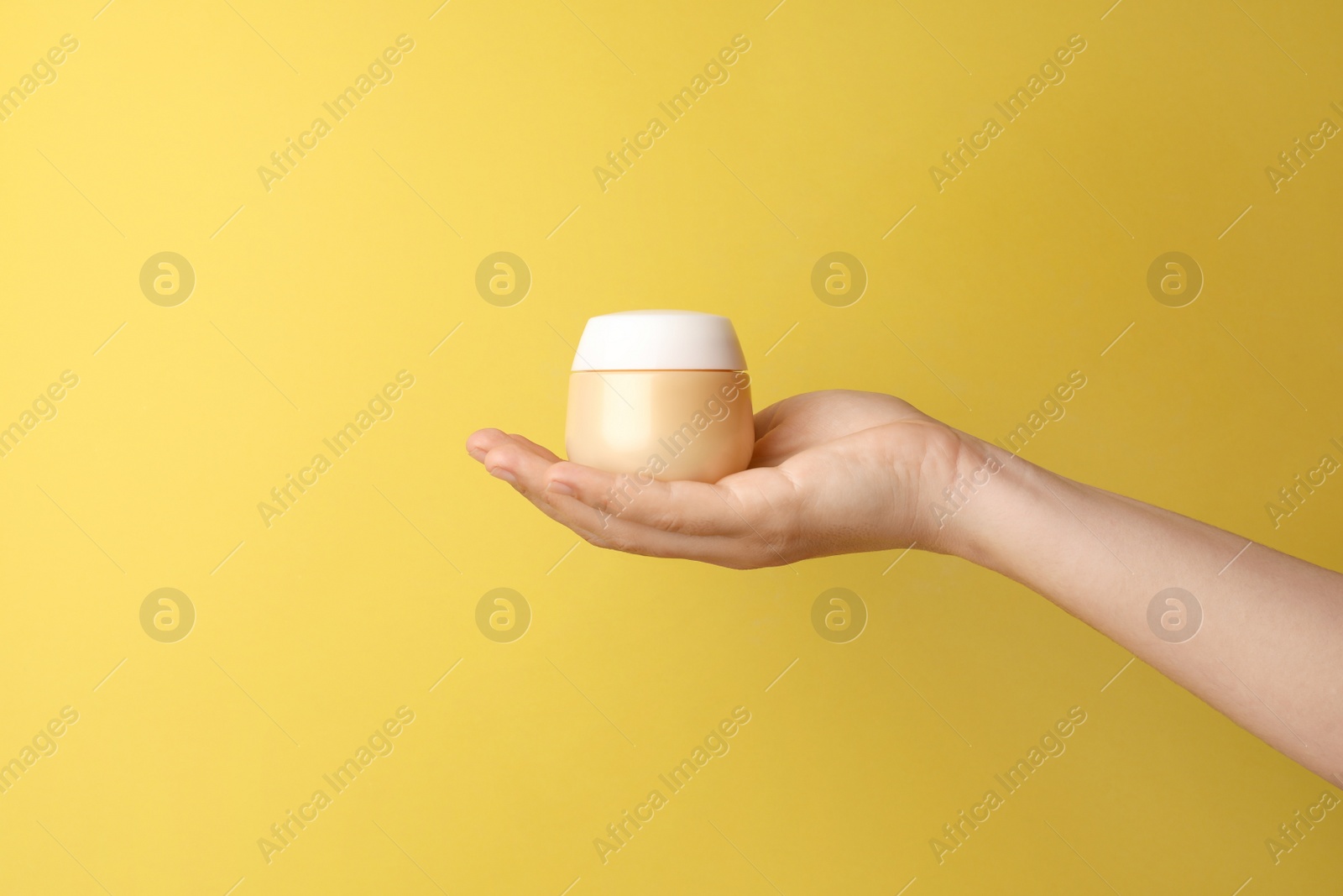 Photo of Woman holding jar of face cream on yellow background, closeup. Space for text