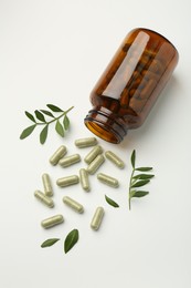 Bottle, vitamin capsules and leaves on white background, flat lay