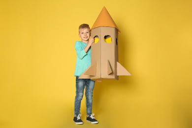 Little child playing with rocket made of cardboard box on yellow background