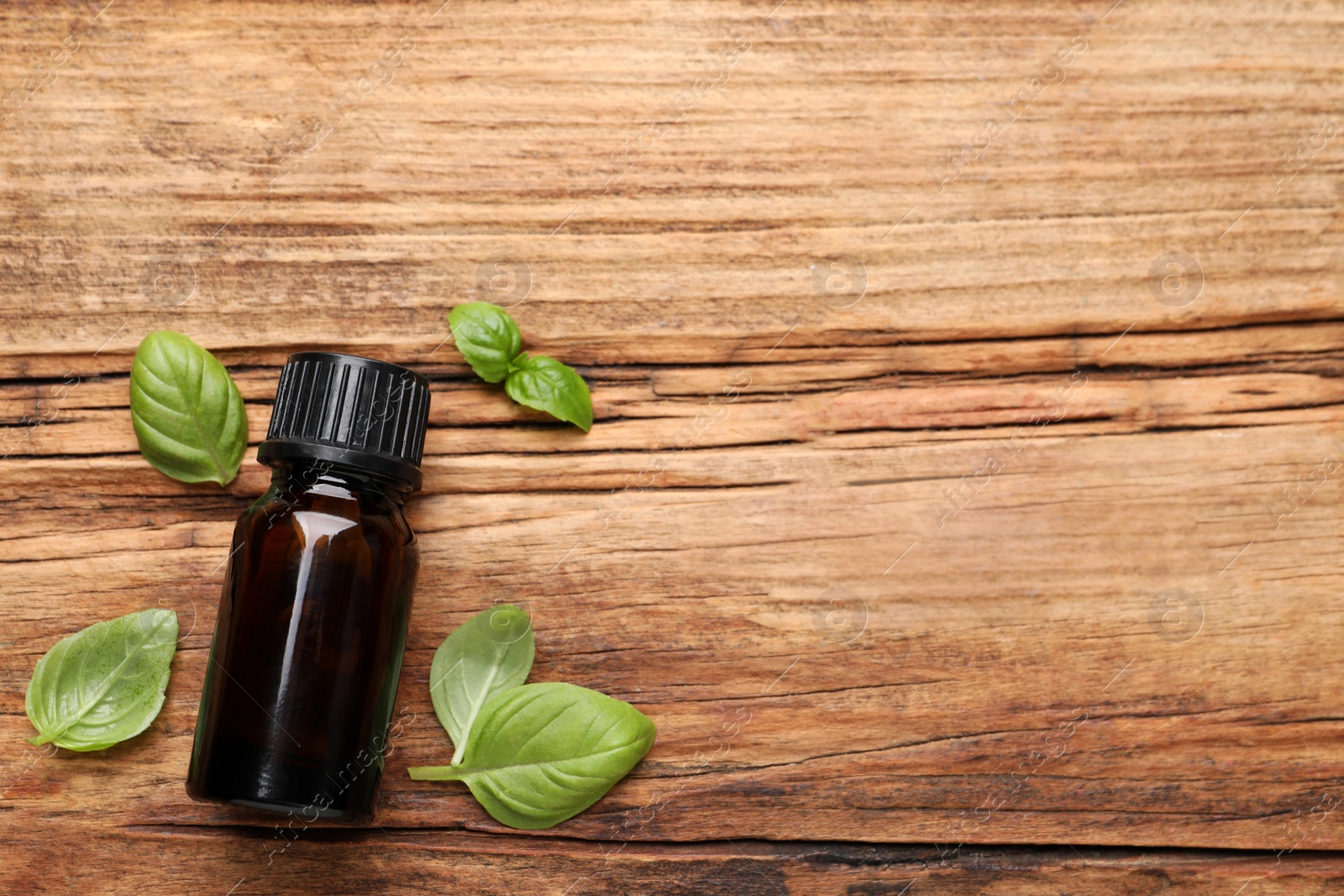 Photo of Glass bottle of basil essential oil and leaves on wooden table, flat lay. Space for text