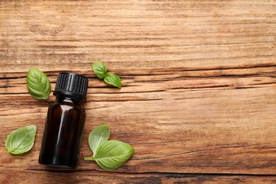 Photo of Glass bottle of basil essential oil and leaves on wooden table, flat lay. Space for text