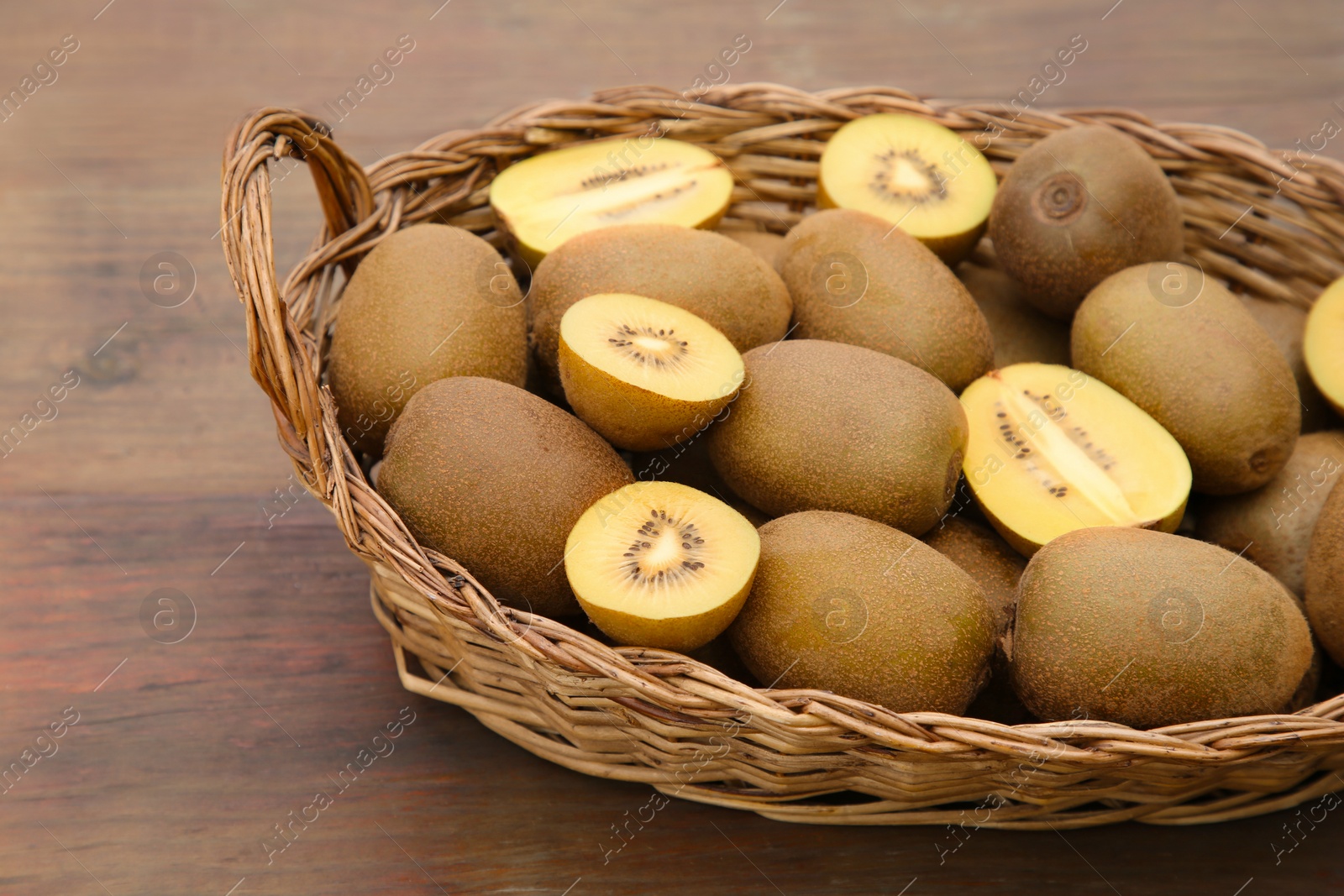 Photo of Basket of many whole and cut fresh kiwis on wooden table, closeup