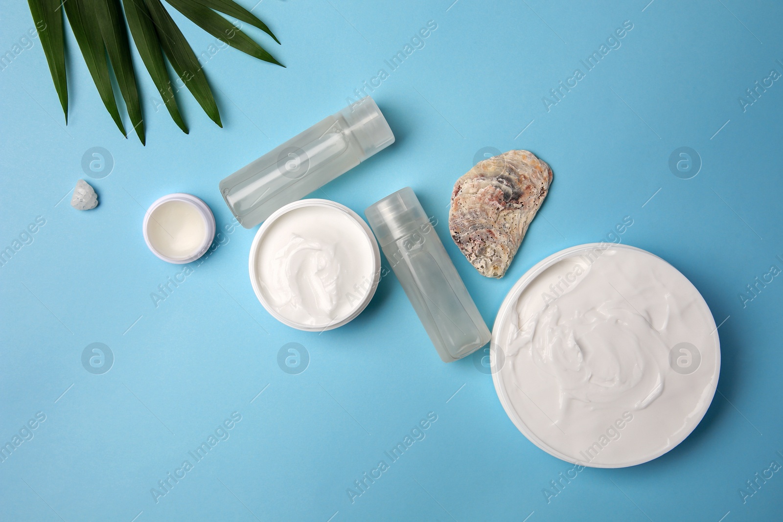 Photo of Flat lay composition with different cosmetic products and palm leaves on light blue background