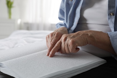 Photo of Blind senior person reading book written in Braille indoors, closeup