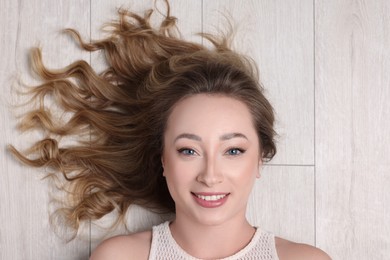 Photo of Portrait of smiling woman with curly hair on wooden floor, top view