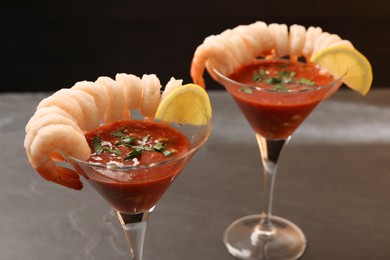 Tasty shrimp cocktail with sauce in glasses and lemon on grey table, closeup