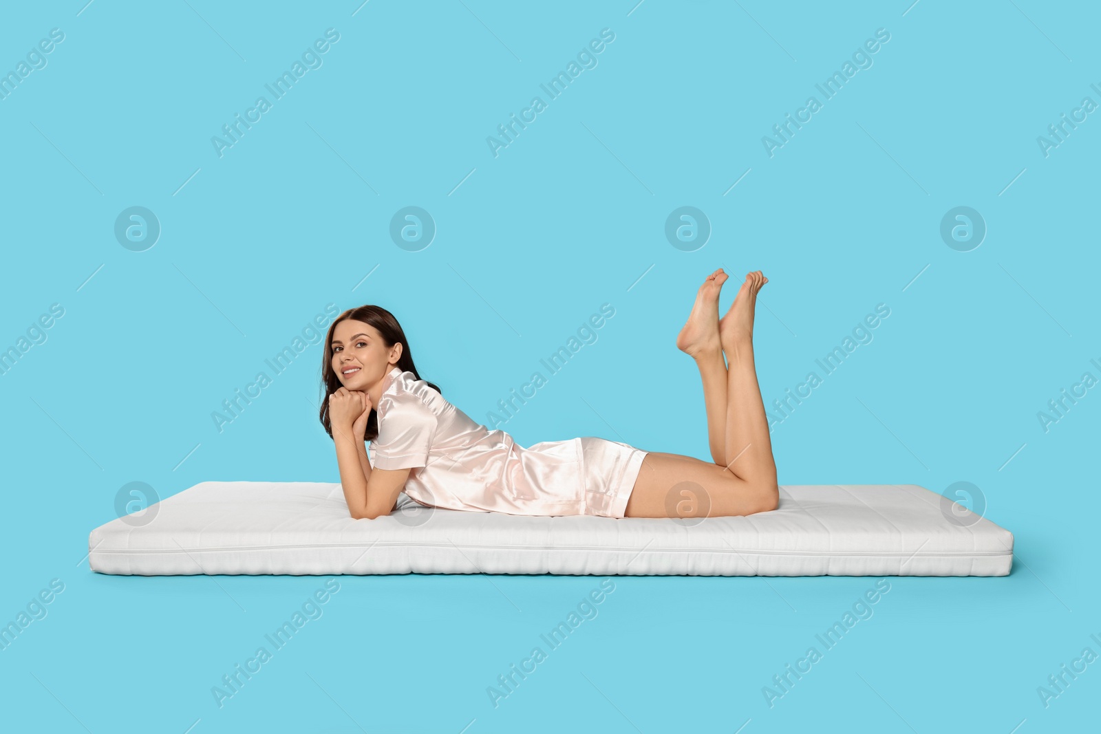 Photo of Woman lying on soft mattress against light blue background