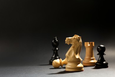 Photo of Different chess pieces against dark background, focus on white knight. Space for text