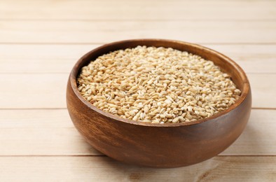 Photo of Dry pearl barley in bowl on light wooden table
