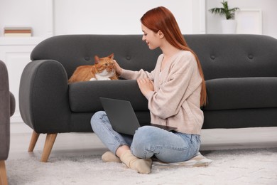 Photo of Woman stroking cat while working with laptop at home