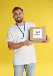 Photo of Male courier holding parcel with sticker Free Delivery on yellow background