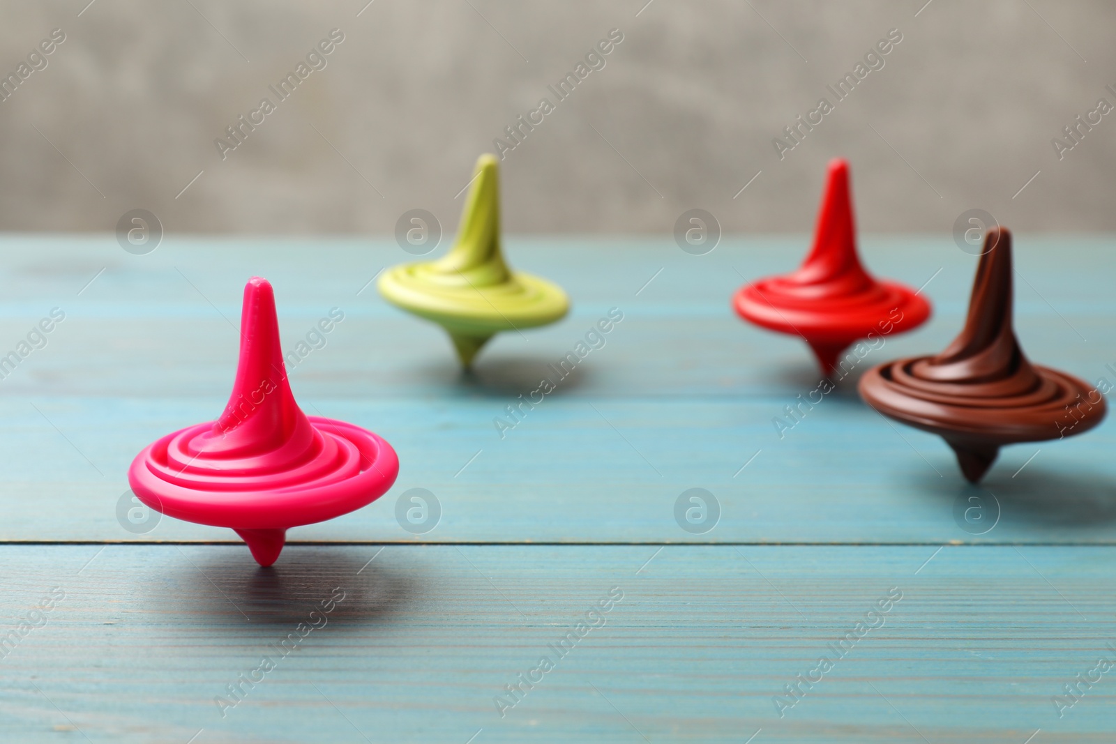 Photo of Bright spinning tops on light blue wooden table, closeup