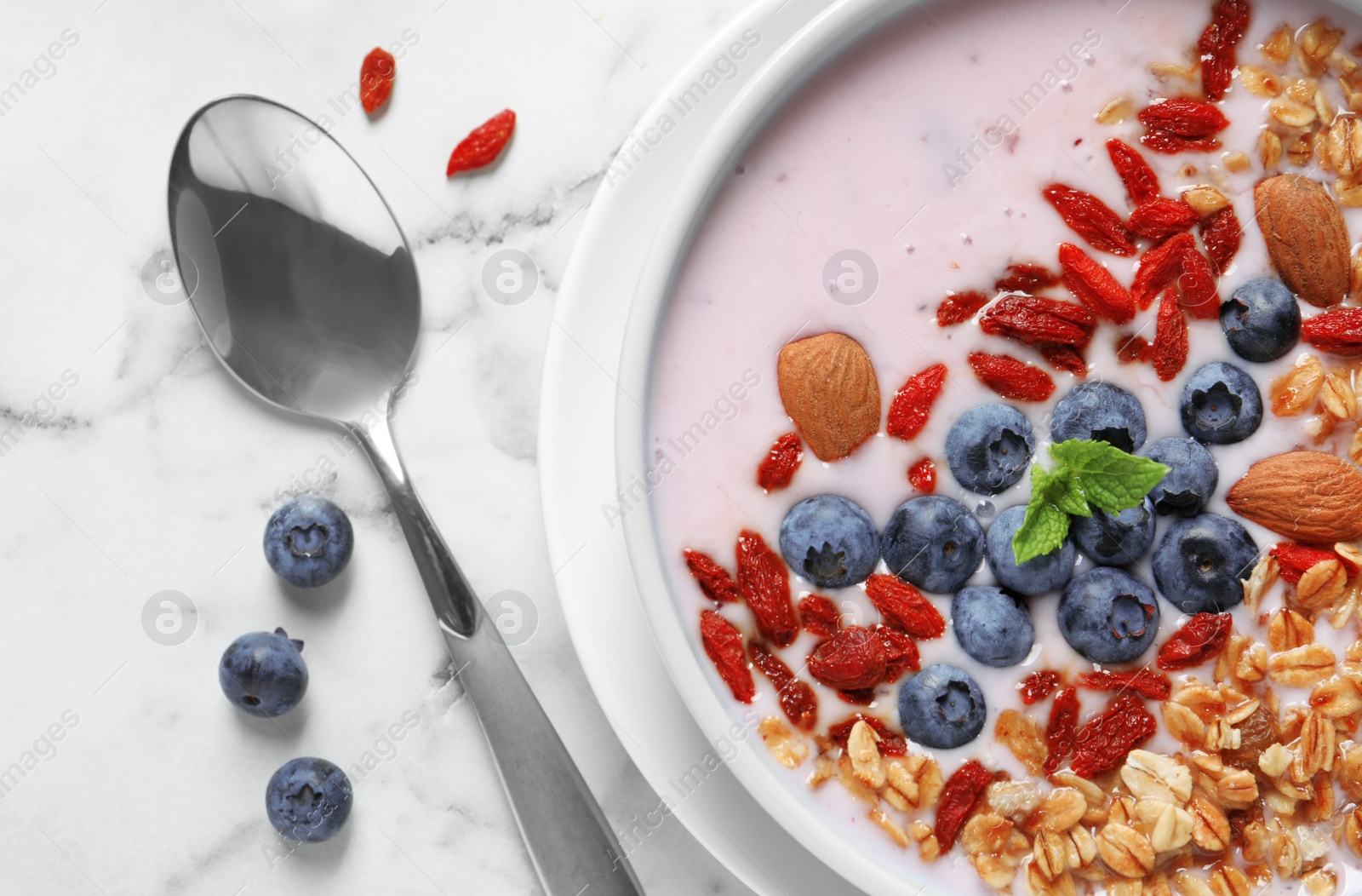 Photo of Smoothie bowl with goji berries and spoon on marble table, closeup