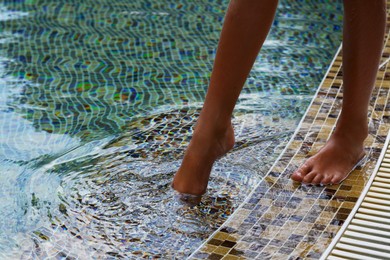 Child testing water temperature in swimming pool with foot, closeup
