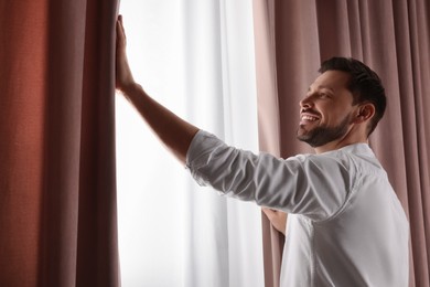 Photo of Happy man opening window curtains at home